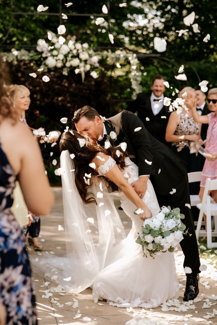 a bride and groom kiss as they walk down the aisle with petals in the air