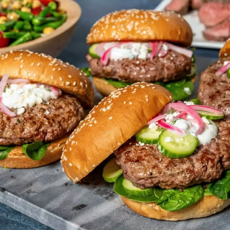 three hamburgers with lettuce, tomato and cucumber on them sitting on a tray