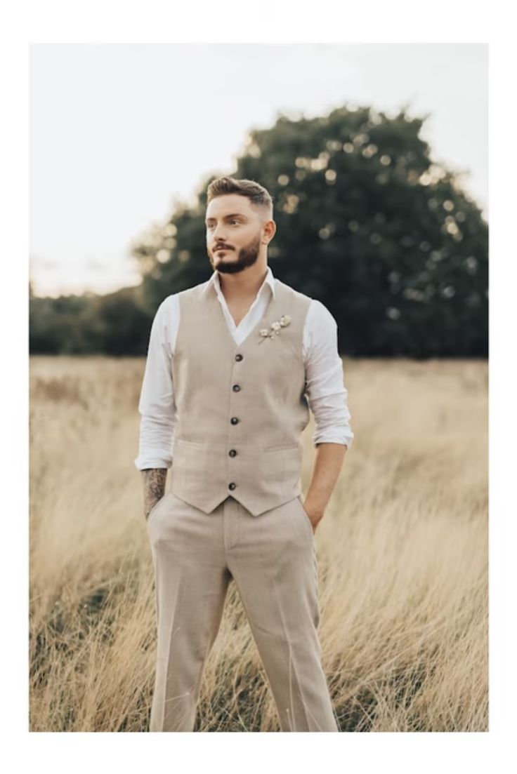 a man standing in tall grass wearing a tan suit