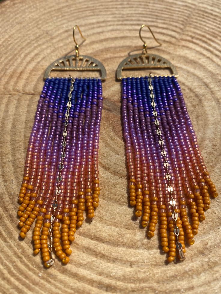 Solstice Skies🌅 For my Wild Hearts who love gazing at the summer sun as it dips below the horizon, you will love these Solstice Skies earrings. The gold colored base along with the sunset colors of blues, purples, pinks and yellows just melt together seamlessly. These beauties are 4 inches long and have gold-plated stainless steel ear wires and boast a sparkly gold chain down the middle. Summer Gold Beaded Nickel-free Earrings, Gold Beaded Nickel-free Earrings For Summer, Gold Beaded Earrings For Summer, Summer Festival Orange Earrings, Purple Earrings For Summer Beach, Summer Festival Gold Beaded Earrings, Summer Rainbow Beaded Earrings, Orange Adjustable Beaded Earrings For Festival, Adjustable Orange Beaded Earrings For Festival