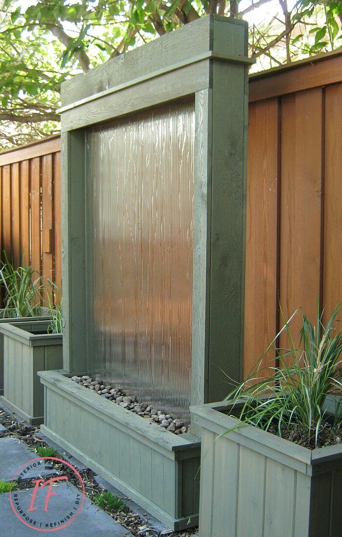 a water fountain surrounded by two planters in front of a wooden fenced area