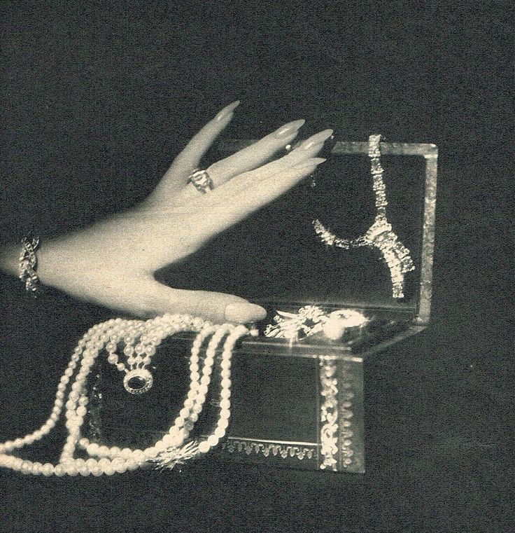 a woman's hand holding onto an open box with pearls and jewelry on it