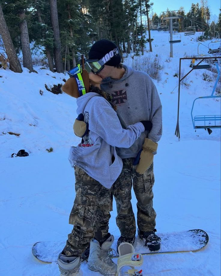 two people kissing on a snowboard in the snow