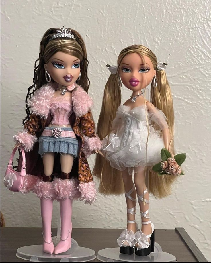 two dolls standing next to each other on top of a table in front of a white wall