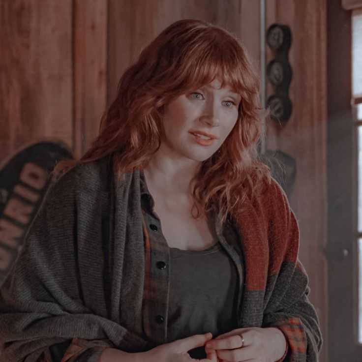 a woman with red hair standing in front of a wooden wall and looking at the camera