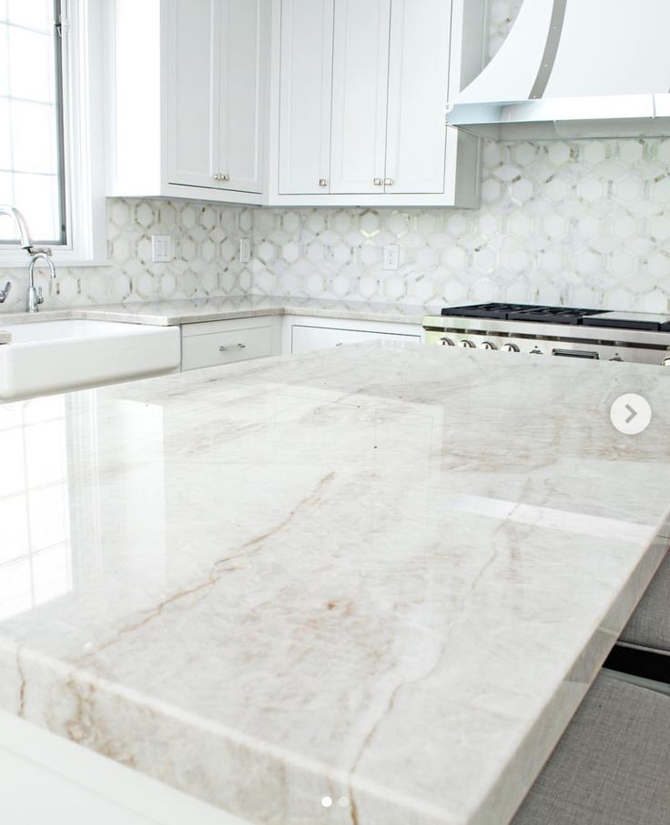 a kitchen with white cabinets and marble counter tops