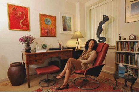 a woman sitting in a red chair next to a book shelf