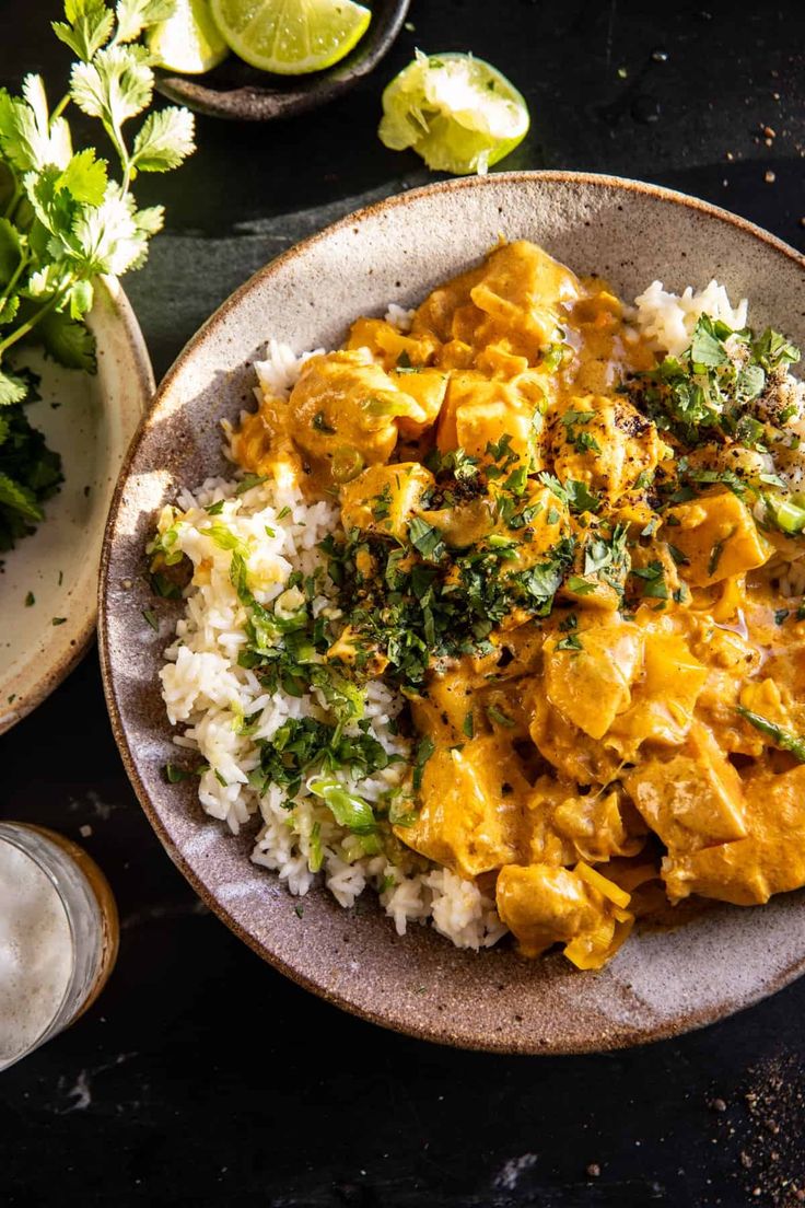 a bowl filled with rice and chicken curry next to some cilantro, lime wedges