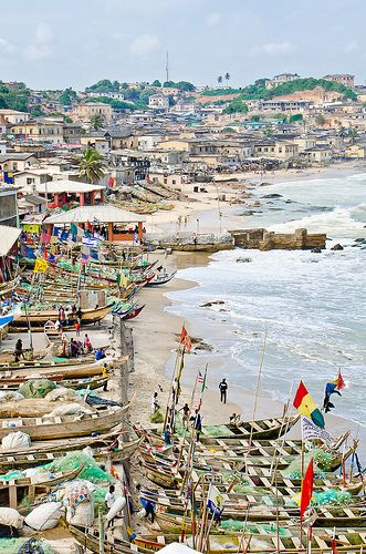 boats are lined up on the beach next to the water and buildings in the background