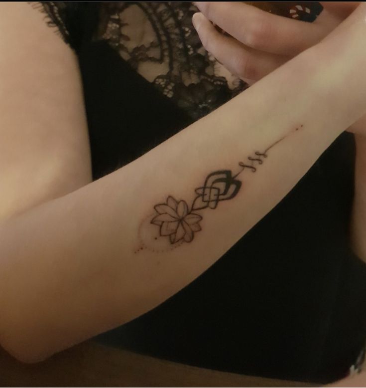 a woman with a flower tattoo on her arm holding a cell phone in her hand