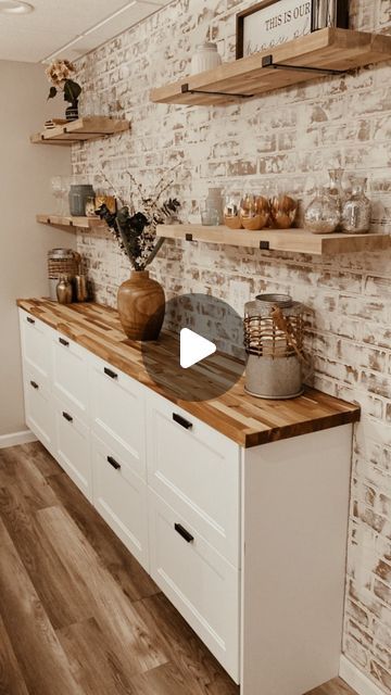 a kitchen with white cabinets and wooden counter tops in front of a brick wall that has shelves on it