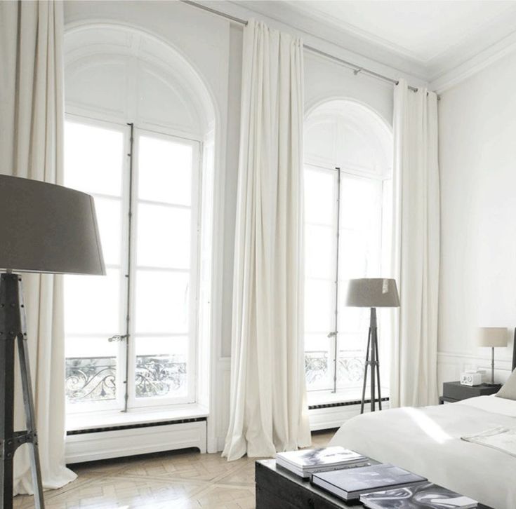 a white bedroom with large windows and curtains