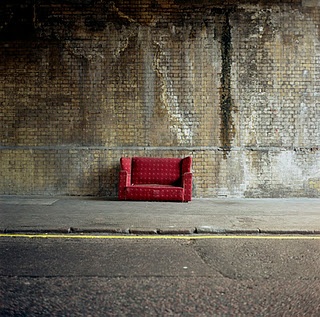 a red chair sitting on the side of a road next to a brick wall with graffiti