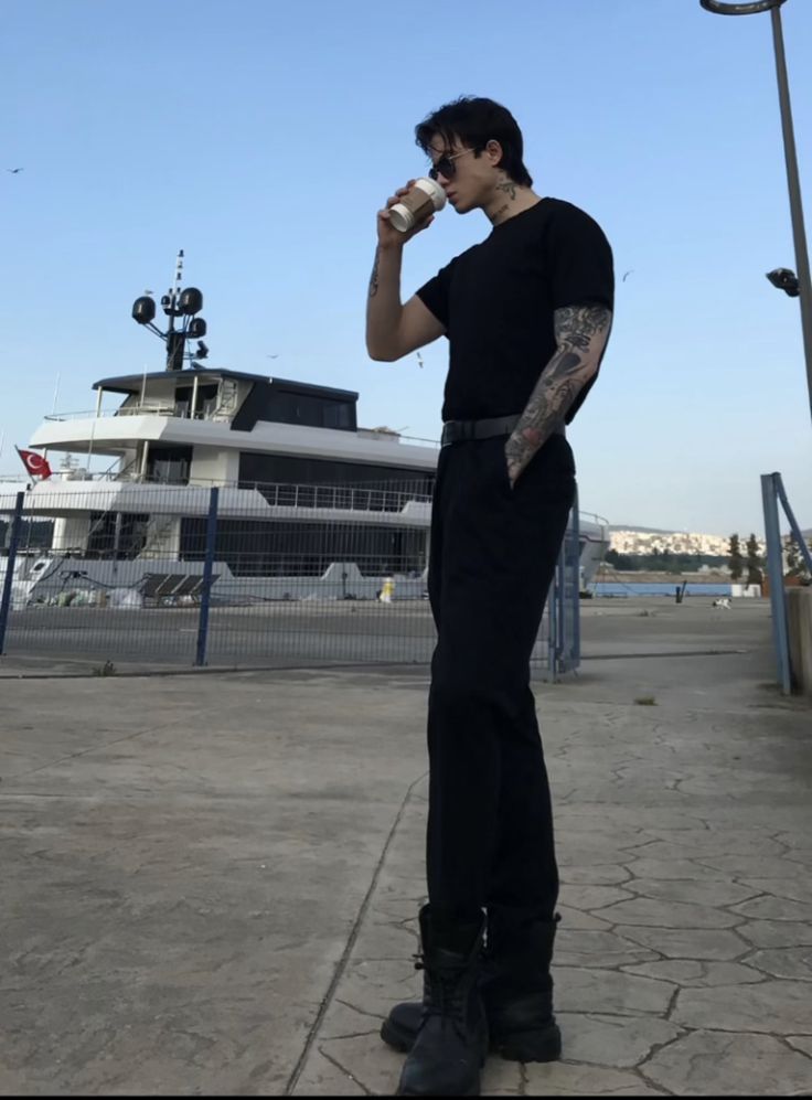 a man standing in front of a boat on the water drinking from a coffee cup