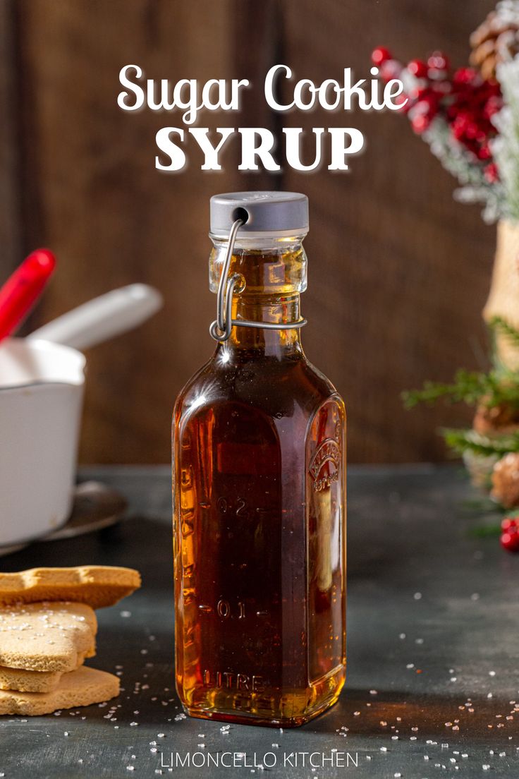 A bottle of Sugar Cookie Syrup on a countertop with sugar cookies to the left of the bottle. The bottle is capped with a grey colored cap. In the background are a white pot with a red spatula in it and some evergreen and berry holiday decorations. Overlay text above the bottle reads “Sugar Cookie Syrup”. Sugar Cookie Syrup, Caramel Cocktail, Coffee Bar Party, Homemade Coffee Syrup, Syrup Labels, Almond Milk Latte, Simple Syrup Cocktails, Flavored Water Recipes, Homemade Sugar Cookies