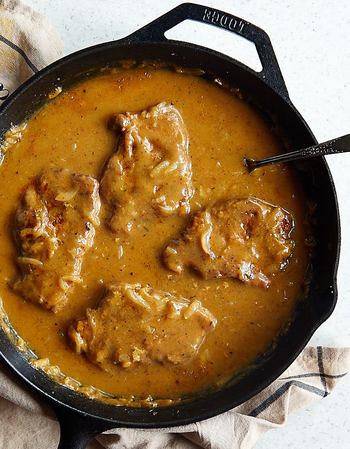 a skillet filled with meat and gravy on top of a white table