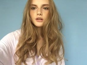 a woman with long blonde hair standing in front of a blue wall