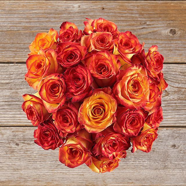 a bouquet of red and yellow roses on a wooden table with planks in the background