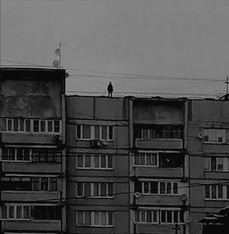 a black and white photo of an apartment building with people standing on the top floor