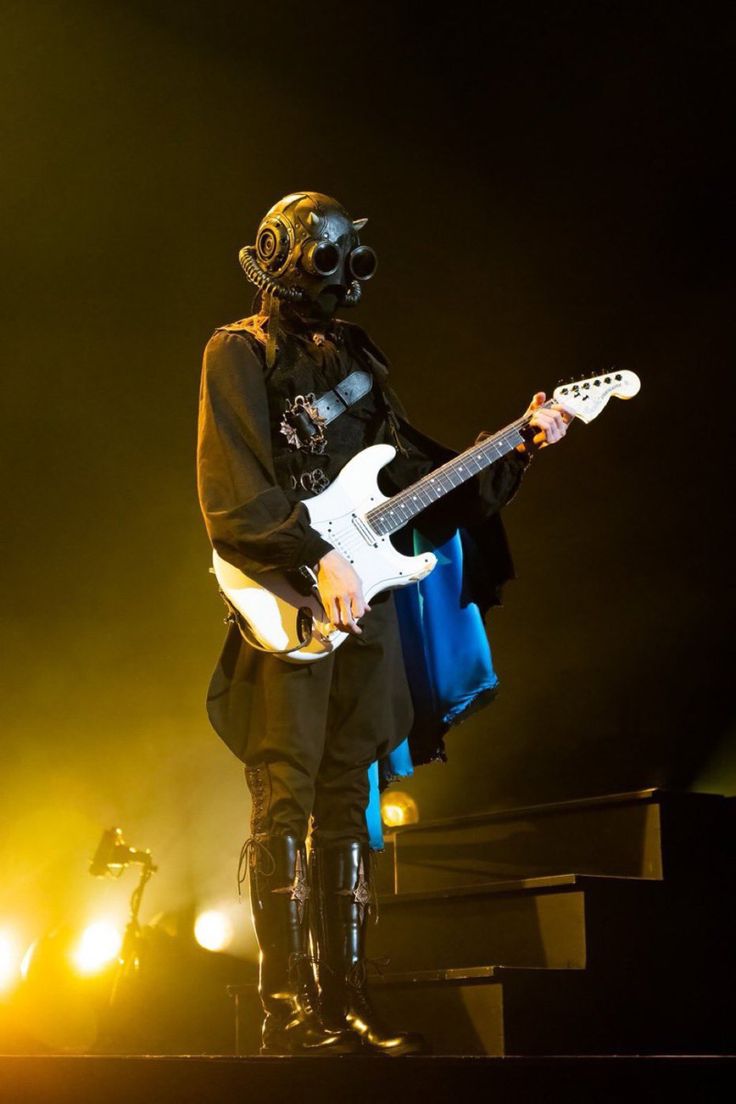 a man in a gas mask playing an electric guitar on stage with his mouth open