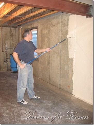 a man holding a large pipe in an unfinished room with concrete walls and exposed ceiling