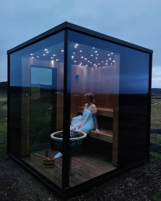 a woman sitting in a sauna on top of a wooden deck next to a field