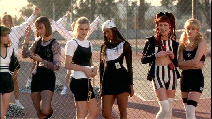 group of young women standing next to each other in front of a chain link fence