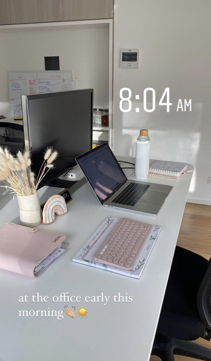 an office desk with a laptop, keyboard and mouse on it in front of a clock