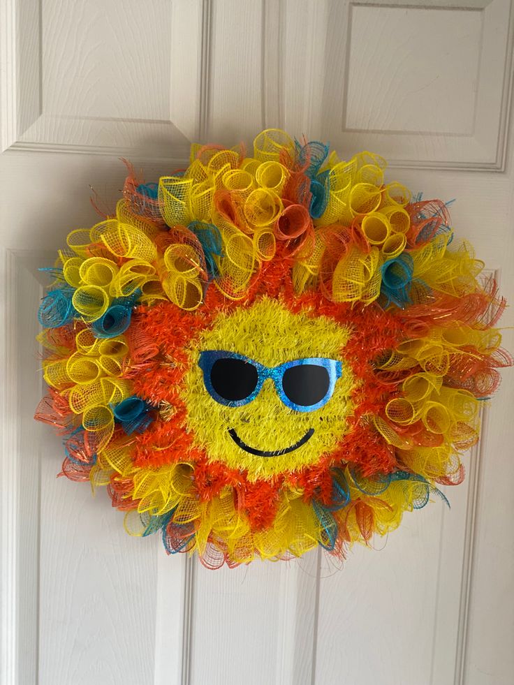 a yellow and orange wreath with sunglasses on it's face is hanging on the front door