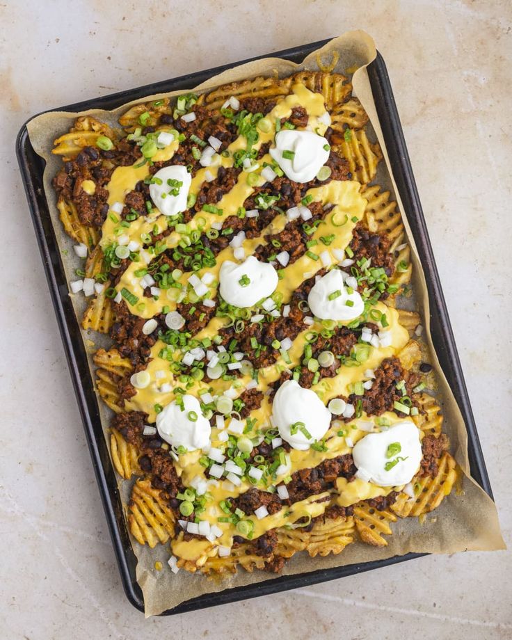 an overhead view of a cheesy pasta dish on a baking sheet with sour cream and green onions