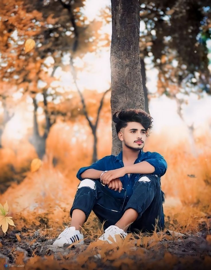 a young man sitting under a tree in the woods with his arms crossed and looking at the camera