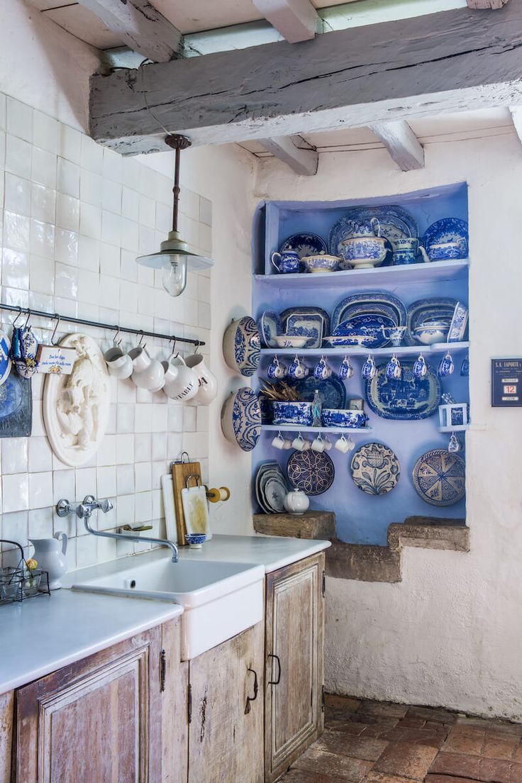 an old kitchen with blue and white dishes on the shelves above the sink, along with hanging utensils