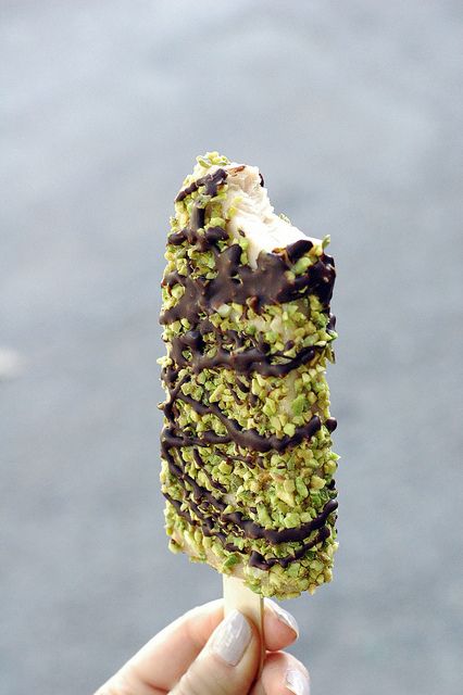 someone is holding up an ice cream cone with chocolate and pistachio toppings