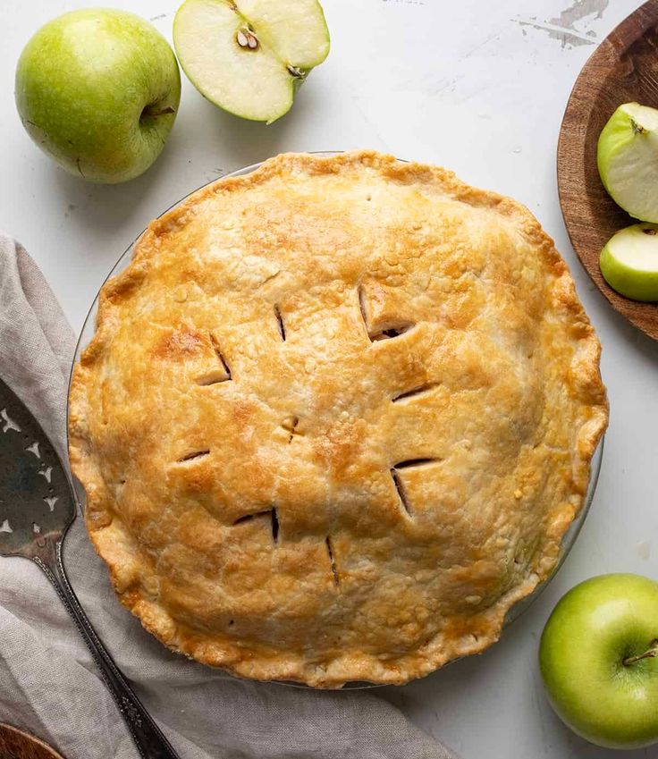 an apple pie on a table with apples around it