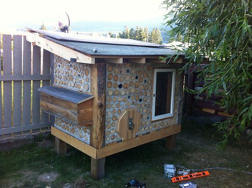 a chicken coop built into the side of a fenced in yard with tools on the ground