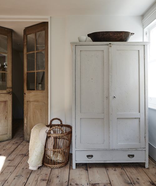 a white cabinet sitting next to a basket on top of a wooden floor in a room