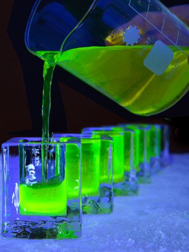 a person pouring liquid into four glasses filled with green liquid on top of a table