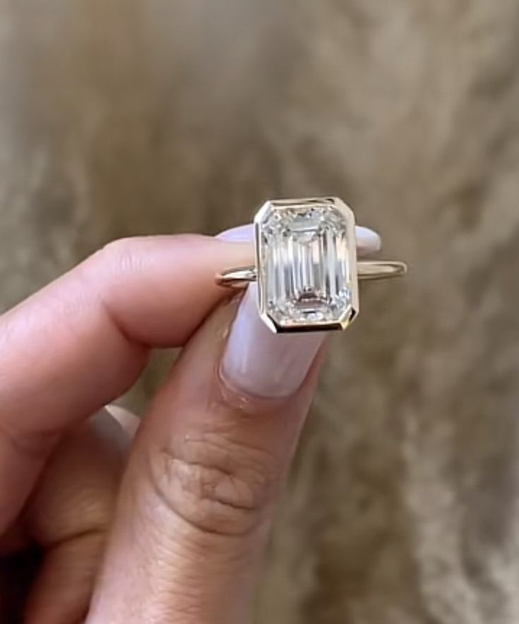 a woman's hand holding an engagement ring in front of her face, with the center diamond on it