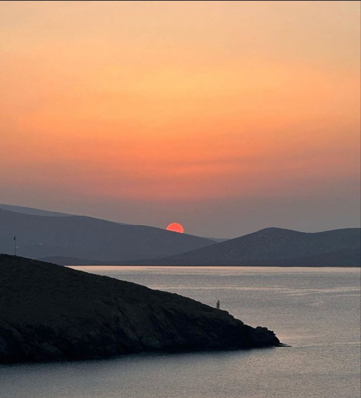 the sun is setting over water with hills in the background