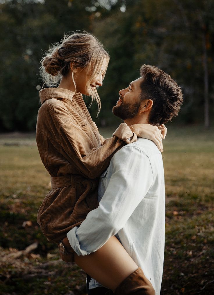 a man holding a woman on his back in a field with trees and grass behind him