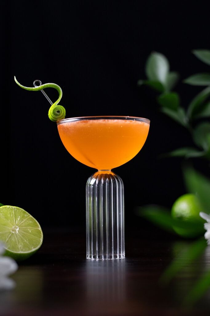 an orange cocktail garnished with a green snake