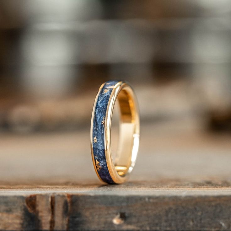 a wedding ring with blue and gold inlays on it sitting on a piece of wood