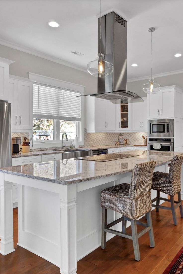 a kitchen with white cabinets and an island in the middle is lit by two pendant lights