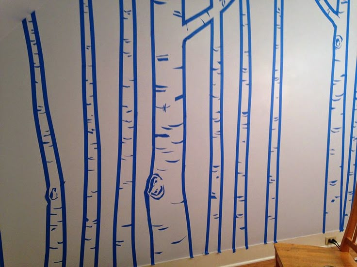 a wall with blue trees painted on it in the corner of a room next to a ladder