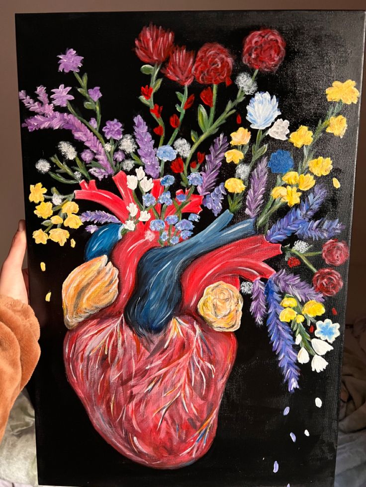 a painting of a human heart with flowers in the center on a black background, held up by someone's hand