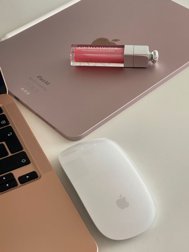 an apple laptop and mouse on a desk with a lip balm stick next to it