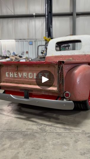 an old red truck parked in a garage next to a white truck with the word chevrolet on it