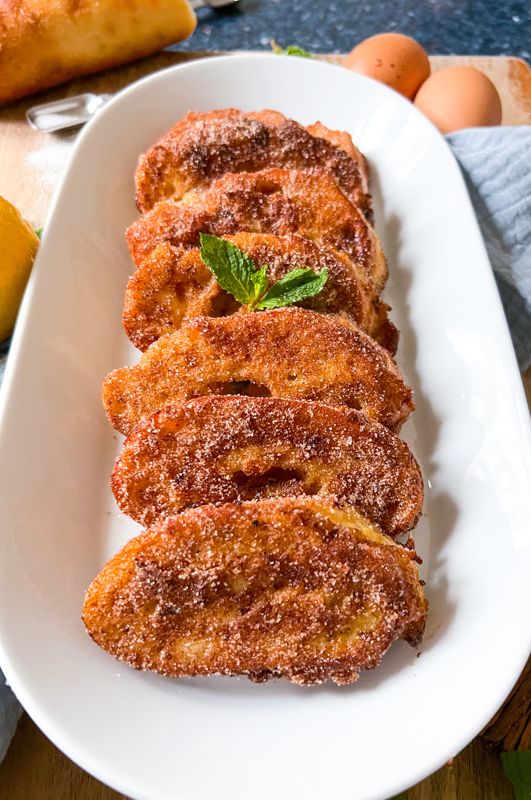 some fried food on a white plate next to eggs and breadsticks in the background