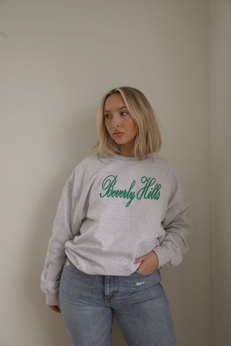 This sweatshirt has a green cursive Beverly Hills graphic on the front. It is made from a soft cotton blend, making it perfect for lounging or running errands in style. Additionally, the sweatshirt is fleece lined for added comfort. embroidered beverly hills ash grey fleece lined crew neck oversized true to size model is wearing a s/m. Height is 5'4", Bust is 33", Waist 28", and Hips 42" wearing sizes 6-8. Fall Sweats With Embroidered Logo For Loungewear, Fall Loungewear Sweats With Embroidered Logo, Winter Loungewear Sweats With Embroidered Logo, Green Long Sleeve Sweatshirt With Embroidered Logo, Sporty Green Cozy Fit Sweatshirt, Green Cozy Fit Sporty Sweatshirt, Long Sleeve Sweatshirt With Embroidered Logo For Loungewear, Long Sleeve French Terry Sweatshirt With Embroidered Logo, Green Varsity Long Sleeve Sweatshirt