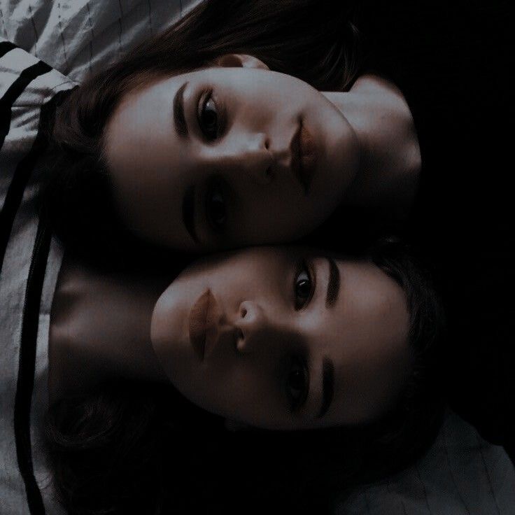 two young women laying on top of each other in the middle of a dark room